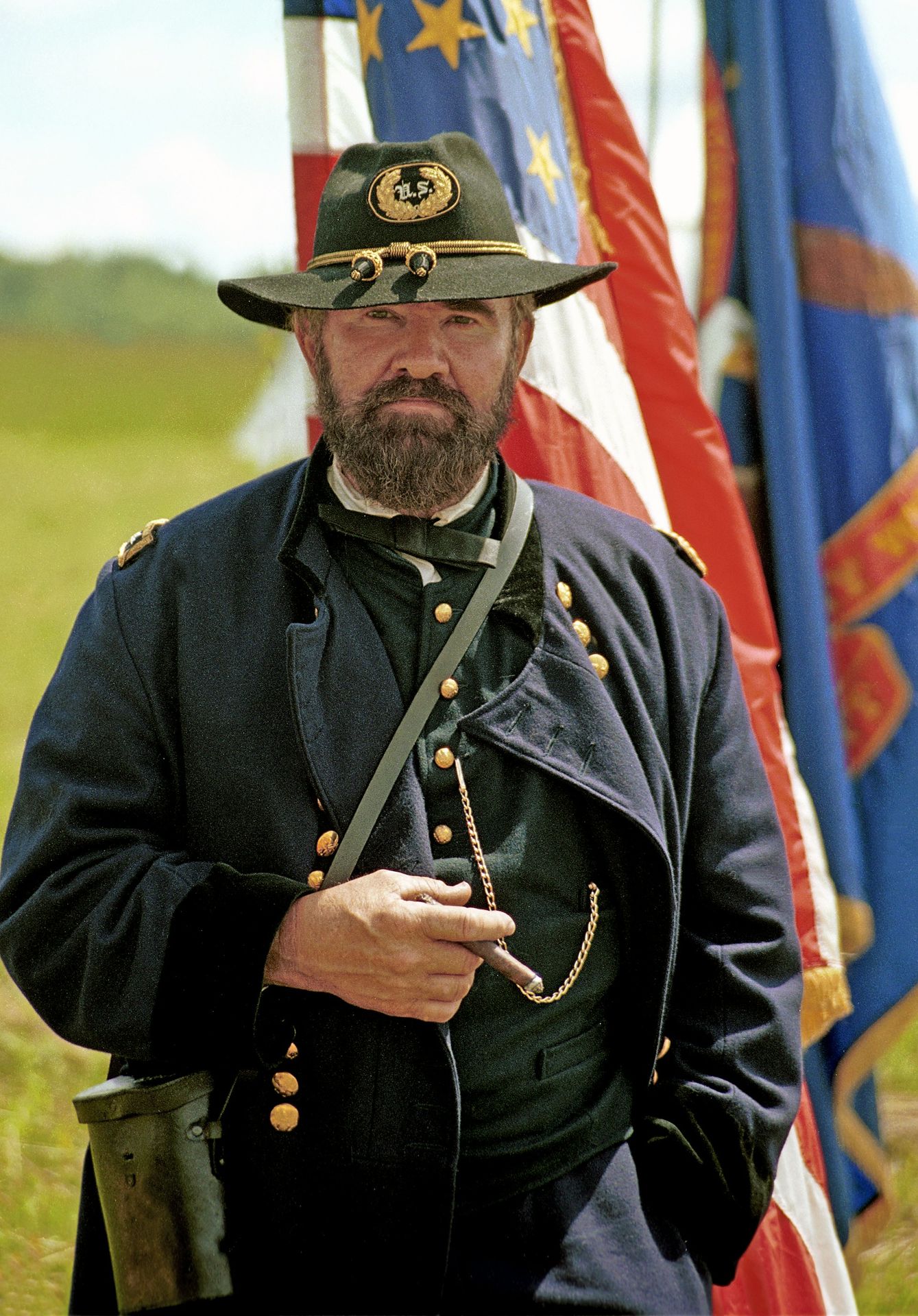 A civil war reenactor poses with flags and a cigar.