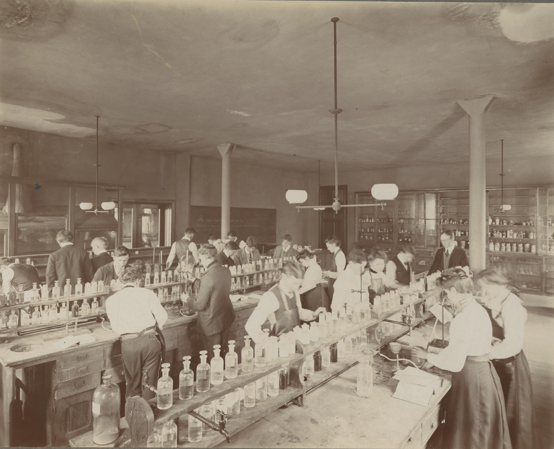 Students working at benches in an early 1900s chemistry laboratory